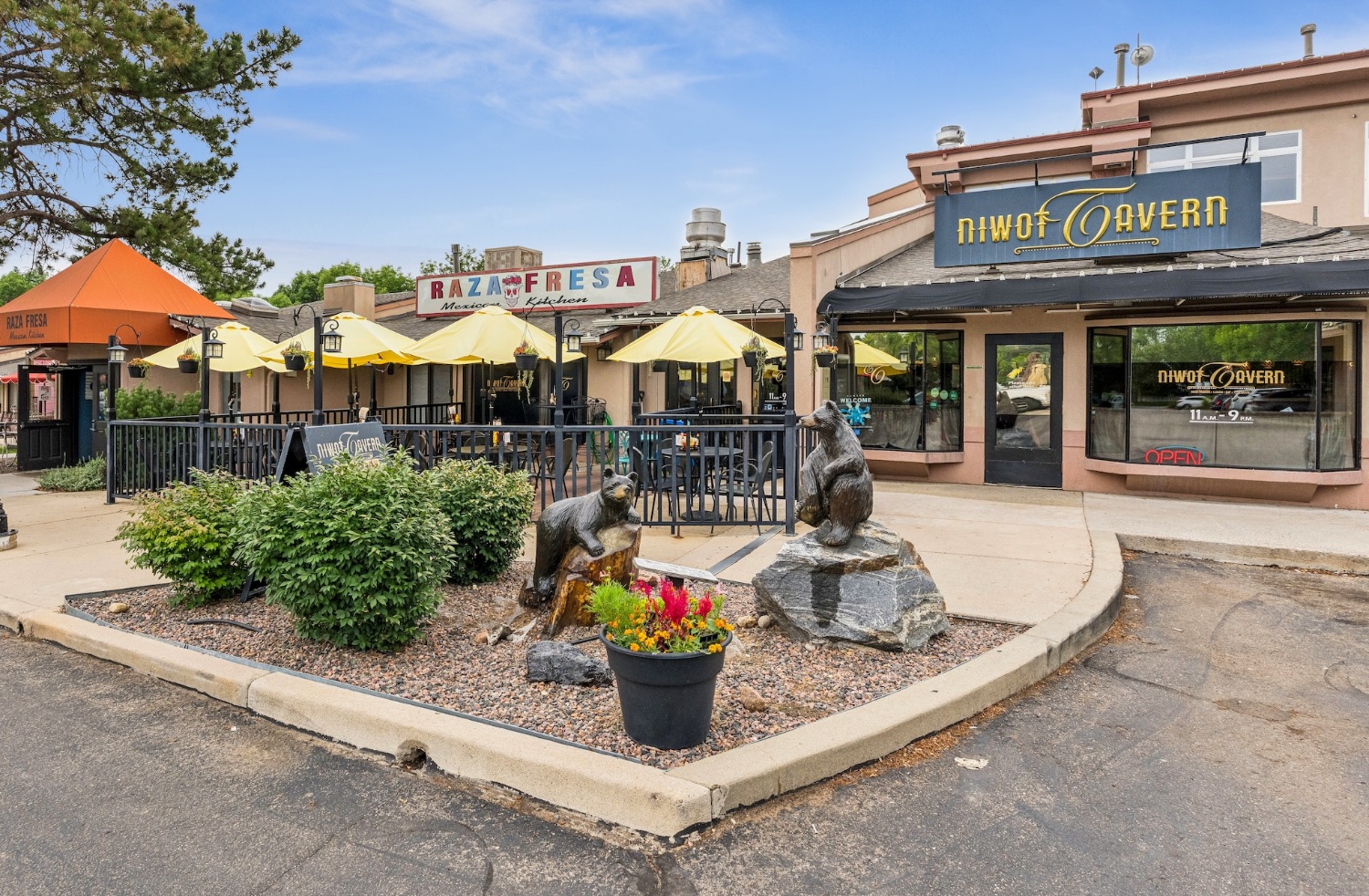 Umbrella-shaded patios outside the Niwot Tavern and Raza Fresa Mexican Kitchen with two bronze bear sculptures on the corner